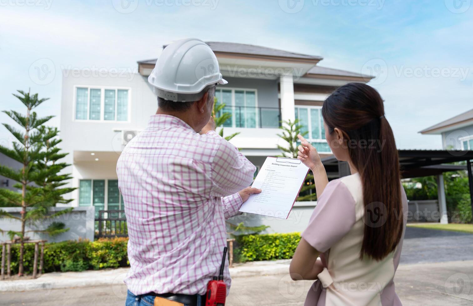 A roof inspector reviews findings with a homeowner in front of a house