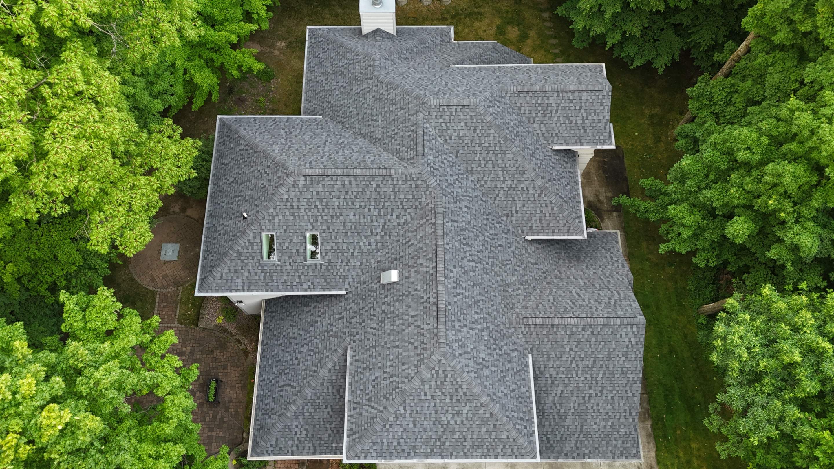 Aerial view of a gray shingle roof surrounded by mature green trees