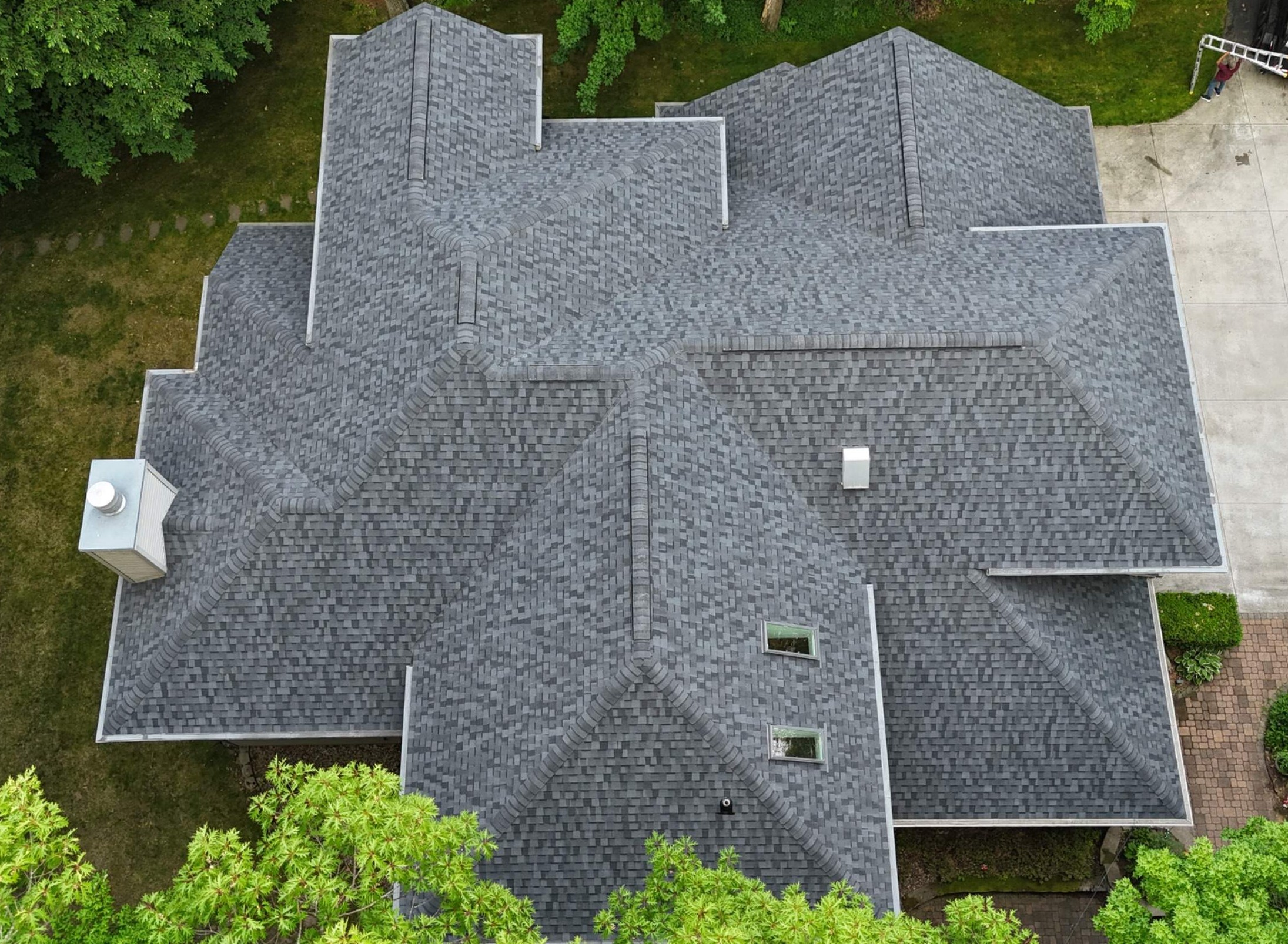 Aerial view of a complex gray shingle roof with multiple ridges, valleys, vents, and skylights
